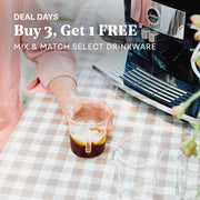 Person holding a glass of iced coffee next to a coffee machine on a picnic table. Promotional text overlayed that reads "Deal Days, Buy 3 Get 1 Free - Mix & Match Select Drinkware."