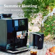 JURA Super Automatic Espresso Machine outside on a picnic table next to a cool connect milk container and coffee. Promotional text overlayed that reads "Summer Hosting - Patio Season Starts Here."