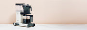 Technivorm Moccamaster in white on a white counter in front of a light pink background.