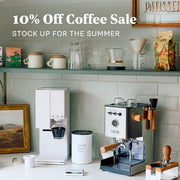Gaggia Classic UP in stainless steel with olive wood accents on a counter next to a xBloom machine and other coffee accessories. Promotional text overlayed that reads "10% Off Coffee Sale - Stock up for the summer".
