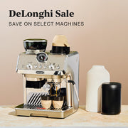 DeLonghi La Specialista on a brown and white counter top next to a vase and coffee canister in front of a beige wall. Promotional text overlayed that reads "DeLonghi Sale - Save on select machines". 