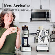 A woman enjoying coffee next to a Lelit coffee bundle on a white counter in a modern kitchen. 