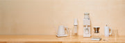 A collection white and clear Varia products on a wooden counter top in front of a beige background.