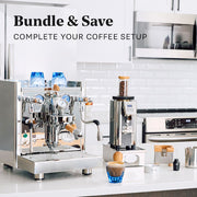 A coffee setup bundle in a bright kitchen setting, featuring a stainless steel espresso machine, a coffee grinder, blue cups, and a prepared coffee cup on a white countertop with text reading 'Bundle & Save'.
