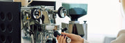 Person holding the portafilter on a Rocket Espresso Appartamento in Anthracite with black panels and a grinder in the background.