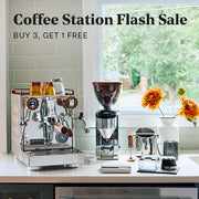 A coffee station setup on a countertop with a stainless steel Rocket Espresso Appartamento, a Rocket Espresso coffee grinder, milk pitcher and scale photographed in a bright kitchen setting with a window and text overlay reading 'Coffee Station Flash Sale BUY 3, GET 1 FREE'.