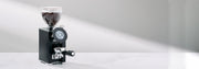 LX Italia Grinder in black with a portafilter on a white counter in front of a gray wall. 