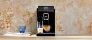 Close-up of a black Gaggia Magenta Prestige and cup of coffee, shown on a countertop against a textured beige wall, with a blue glass next to it.