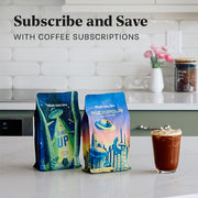 A bag of Whole latte Love Beaned UP and Whole Latte Love Buzzopolis next to a cup of coffee on a white kitchen island. Promotional text overlayed that reads "Subscribe and Save with Coffee Subscriptions".