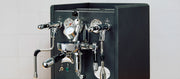 An Anthracite espresso machine with a flow control device against a white marble background.