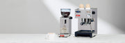 Lelit Anna Espresso Machine next to a Lelit Fred Espresso Grinder and latte cup on a white counter in front of a gray wall.