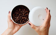 Person holding a container of coffee beans against a white background.