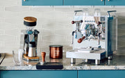 Bezzera Espresso machine next to a Eureka grinder on a kitchen counter with various coffee-making tools.