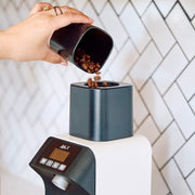 Person pouring coffee beans into a Ceado Life X coffee grinder with a tiled wall background.