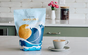 Whole Latte Love Crema Wave next to a latte on a kitchen island with a counter in the background.