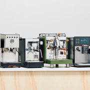 Four espresso machines of different models on a wooden surface with a light gray background.