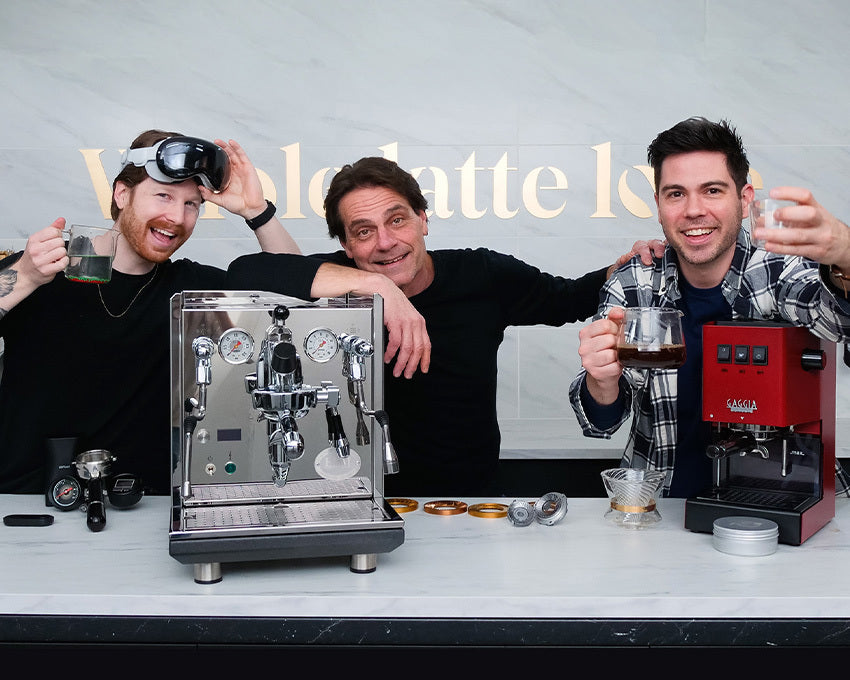 Three men posing with an ECM Synchronika and Red Gaggia Classic Pro in a kitchen setting.
