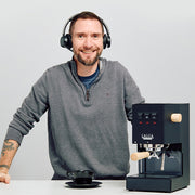 Man with a headset next to a black Gaggia Classic Pro E24 with Tiger Maple accents on a counter.