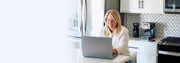 Woman using a laptop in a kitchen with Gaggia Espresso Evolution on the counter behind her. 