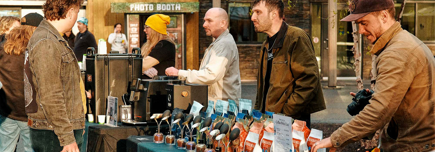 Coffee stand with workers behind a table of different coffee bags and espresso machines.