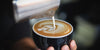 Milk pouring into a latte, with an image of a frond visible in the foam