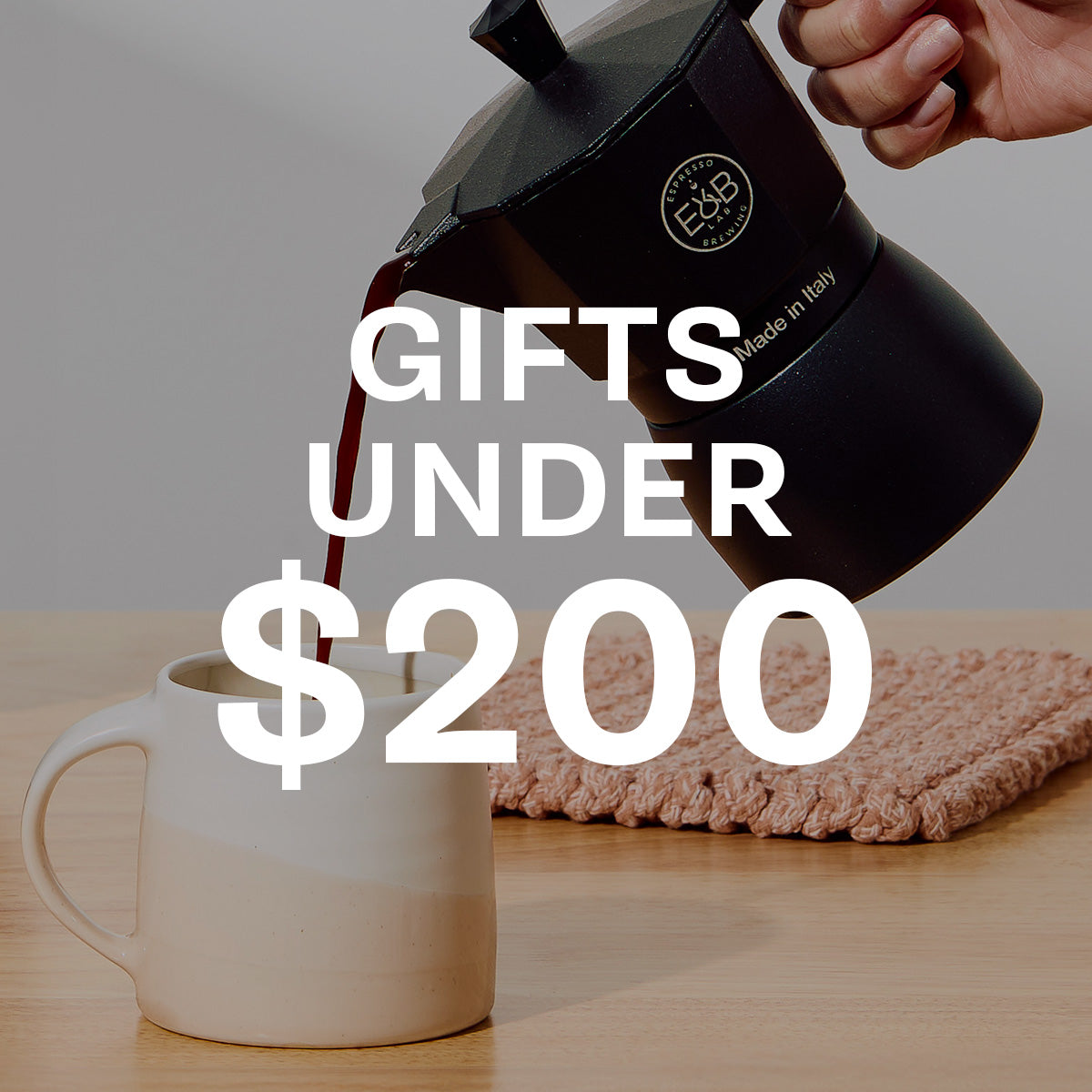 Black E&B Lab coffee maker pouring coffee into a white mug with text 'Gifts Under $200' on a neutral background.