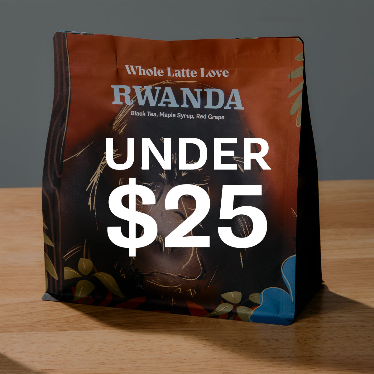 Close-up of Whole Latte Love Rwanda Coffee on a wooden table in front of a gray background. Text overlayed that says UNDER $25.