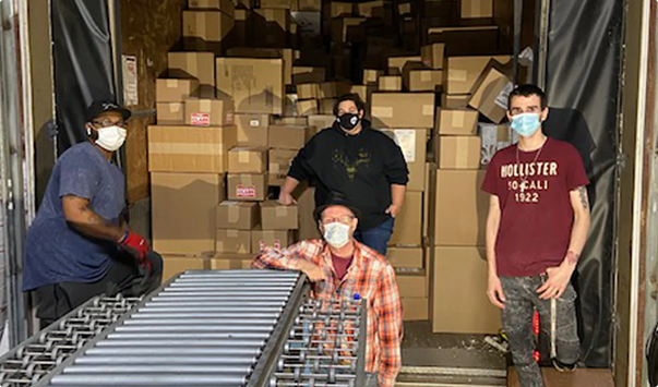 Four individuals working with boxes and a conveyor belt in a warehouse setting.